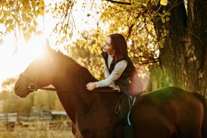 Junge Reiterin und ihr Pferd bei goldigem Sonnenschein